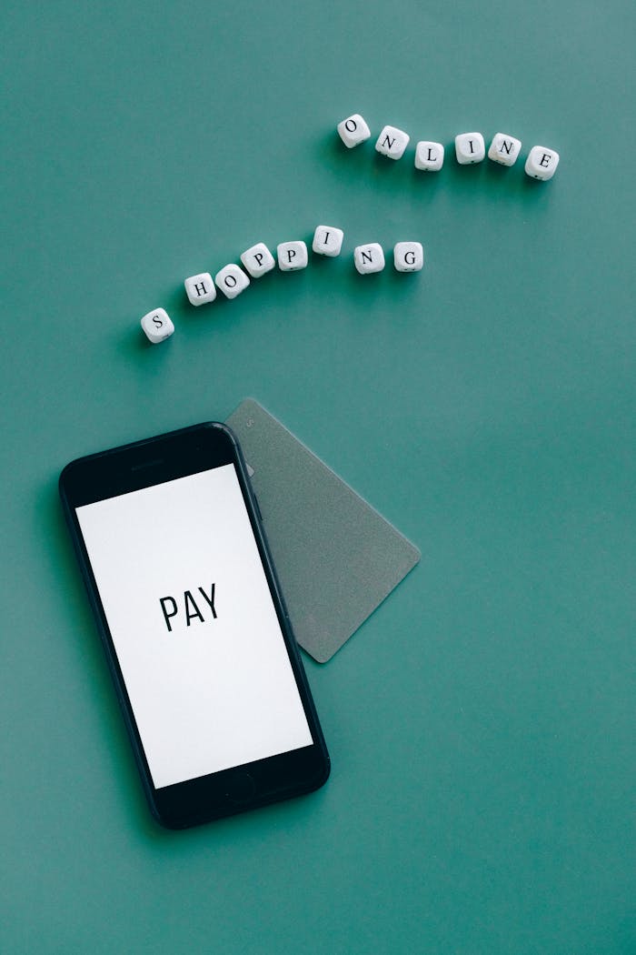 Smartphone with the word Pay displayed alongside a card and letters spelling Shopping Online on a green background.